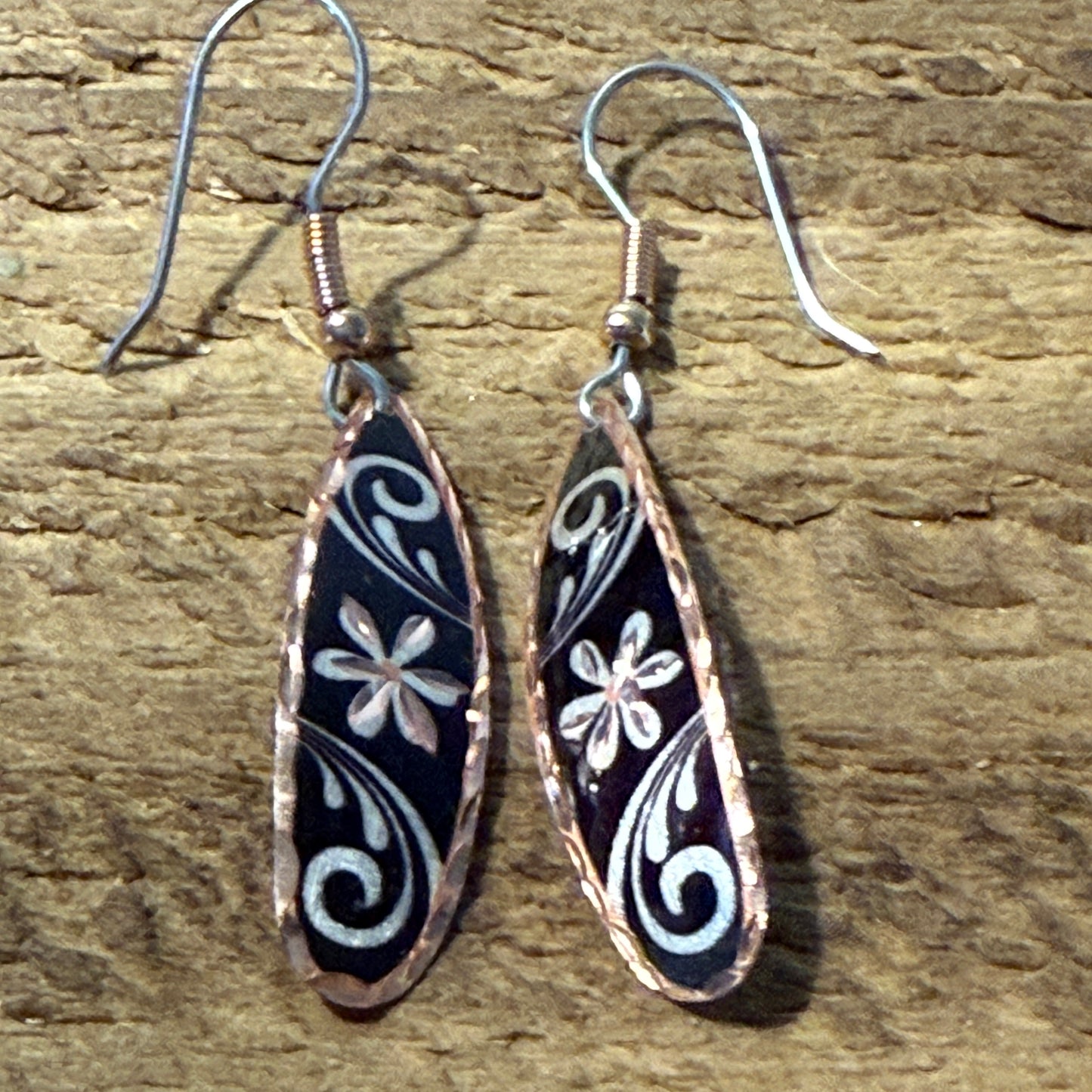 Handcrafted copper rose-gold wire drop earrings with black enamel and white floral swirl patterns.