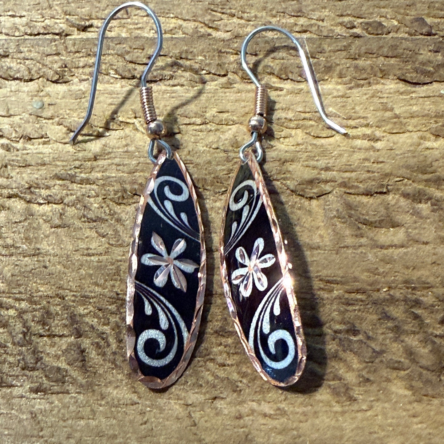 Handcrafted copper rose-gold floral wire drop earrings with black enamel and white floral swirl patterns.