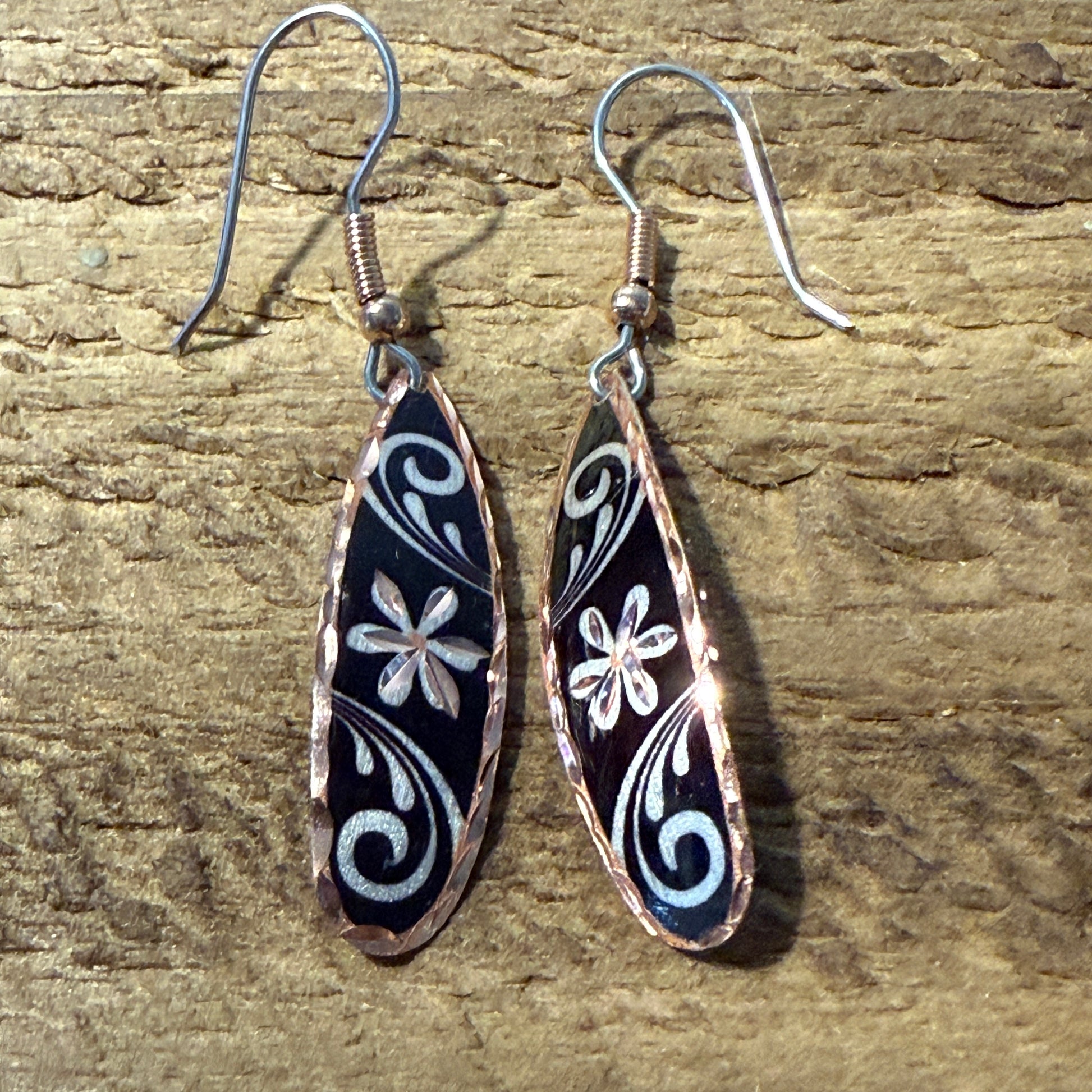 Handcrafted copper rose-gold floral wire drop earrings with black enamel and white floral swirl patterns.